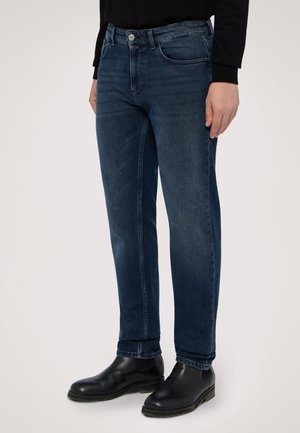 Jeans in denim blu scuro con taglio dritto, dotati di zip, cinque tasche e una leggera sfumatura. Abbinati a stivali neri in pelle sopra la caviglia.