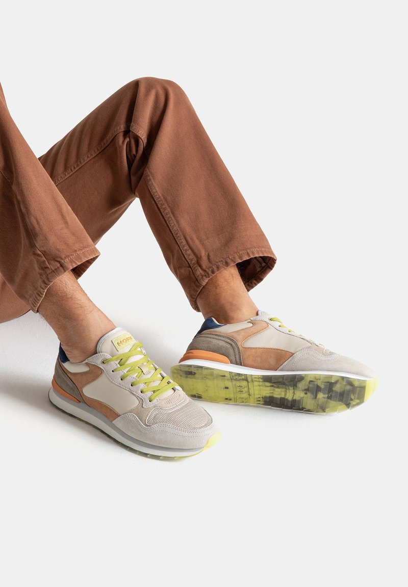 Zapatillas con parte superior de ante y malla en beige y marrón, con cordones verde neón y una suela multicolor. Diseño minimalista con acentos en contraste.