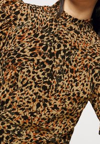Leopardi-kuosiset pusero beigen, mustan ja oranssin sävyissä. Varustettu korkealla kaula-aukolla ja rypytetyillä puffihioilla, valmistettu pehmeästä kankaasta.