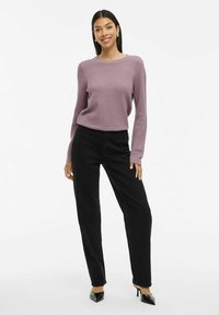 Pull en tricot violet clair avec un col rond, associé à un pantalon noir. Le modèle porte des chaussures à talons noires, affichant une coupe décontractée.