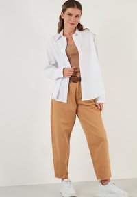 White button-up shirt, beige tank top, tan wide-leg pants, light sneakers, highlights a belt, sleek design, relaxed fit, minimalistic style.