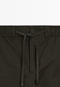 Shorts décontractés vert foncé avec une taille élastique, une fermeture à bouton et un cordon de serrage. Présente une texture lisse et un design simple.