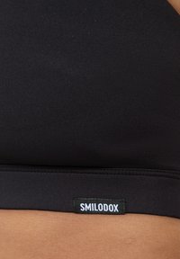 Zwarte sportbeha met een soepele stofstructuur, naadloos ontwerp en een zichtbaar label met de merknaam "SMILODOX" aan de onderkant.