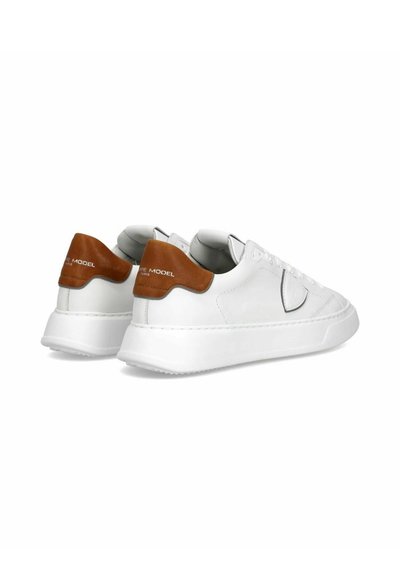 Hvide lædersneakers med en brun læderdetalje ved hælen. Tykk hvid gummisål, snørebåndsdesign og en glat overflade.