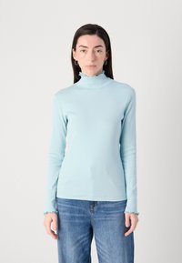 Lichtblauw, langekiel turtleneck shirt met een gerimpelde kraag en manchetten, gemaakt van een rekbare ribstof. Gemaakt in combinatie met blauwe spijkerbroek.