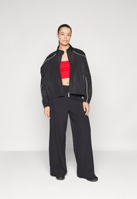 Zwarte windjack met witte accenten, gecombineerd met een rode crop top en zwarte wijde broek, gemaakt van lichtgewicht, ademend materiaal.
