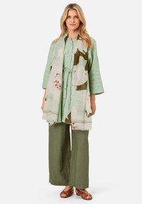Light green linen shirt, olive green wide-leg pants, and a patterned scarf with greens and reds; relaxed fit, textured fabric, and fringe detail.