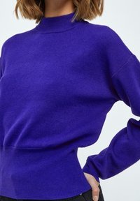 Suéter morado de cuello alto con mangas largas, fabricado en suave tejido de punto, cuenta con una cintura ceñida y un corte holgado y relajado.