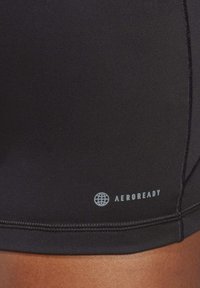 Svarte treningsshorts laget av glatt stoff, med flate sømmer og en liten "AEROREADY"-logo i lys grå på siden.