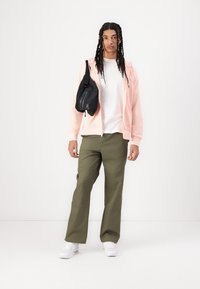 Casaco de capuz rosa com fecho, t-shirt branca, calças cargo verdes-oliva, bolsa de alça preta, ténis brancos; corte descontraído e design casual.