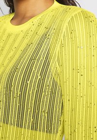 Gul långärmad topp med vertikala randiga spetsdesign. Har inbäddade paljetter för textur och en lätt lyster.