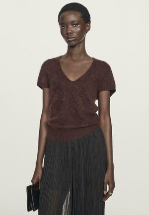 Brown fuzzy short-sleeve sweater with a V-neck design, paired with a long black pleated skirt. The model holds a black clutch.