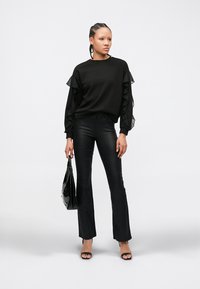 Zwarte top met lange mouwen en gerimpelde mouwen, gecombineerd met zwarte flarebroeken. Accessoires zijn onder meer een glanzende zwarte handtas en zwarte sandaalhakken met bandjes.