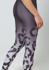 Högmidjade leggings i en gradient grå med mörk leopardmönster, med en mjuk, elastisk textur och kontrasterande söm på sidan.