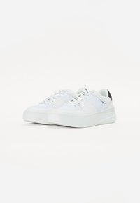 Baskets blanches avec une tige en cuir lisse et texturé, des lacets plats, une semelle plateforme et un accent noir au niveau du talon.