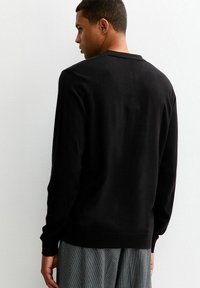 Maglione nero a maglia con maniche lunghe, scollatura rotonda e polsini a costine. Texture liscia. Appare uniforme senza motivi o accenti visibili.