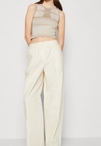 Beige stickad crop top med texturerat mönster och ribbade kanter, parat med vita byxor i vid modell med hög midja och framfåll.