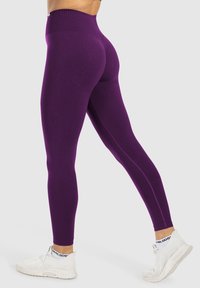 Lila hoch taillierte Leggings aus glattem, dehnbarem Stoff, mit schlankem Schnitt und knöchellangem Design, kombiniert mit weißen Sportschuhen.