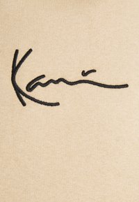 Tessuto beige con superficie testurizzata che presenta un disegno prominente di firma ricamata in nero.