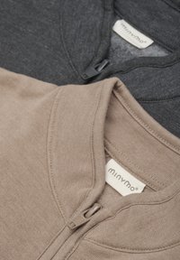 Zwei Reißverschlussoberteile in Grau und Beige, aus weichem Stoff. Sie haben einen hohen Kragen, eine glatte Textur und ein Markenlabel am Hals.