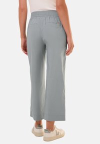 Pantaloni a gamba larga grigio chiaro con vita elastica, due tasche posteriori e una texture liscia. Abbinati a sneakers beige con dettagli.