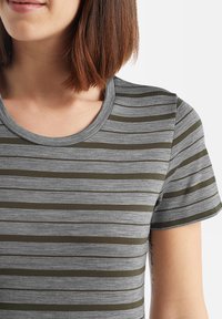 Woman wearing a grey and olive green striped short sleeve t-shirt with a round neckline, showing part of her neck and shoulder.