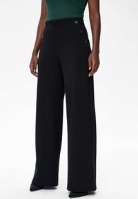 Zwarte wijde broeklegs gemaakt van een soepele stof, met drie decoratieve knopen aan de zijkant en een gepaste pasvorm.