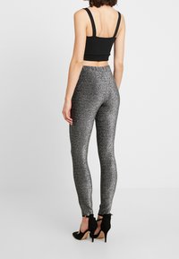 Haut noir crop avec des bretelles épaisses, associé à des leggings ajustés et brillants en argent métallique, dotés d'une texture lisse et d'une taille élastique.
