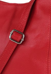 Rode leren handtasriem met een vierkante metalen gesp, een gestructureerde afwerking en zichtbare stiksels. Close-up van strapdetail.