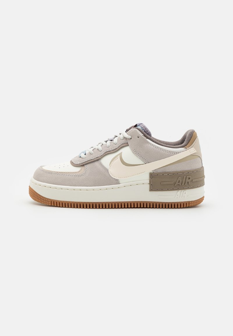 Baskets basses en daim beige et cuir crème, lacets blancs, semelle en gomme et grand logo Nike Swoosh sur le côté.