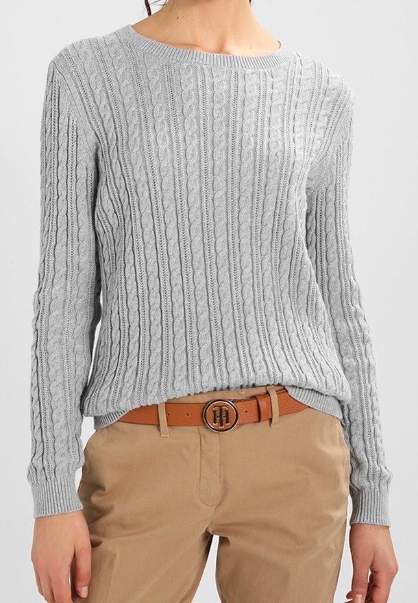 Pull gris clair en maille torsadée associé à un pantalon beige et une ceinture en cuir marron avec une boucle métallique ronde.