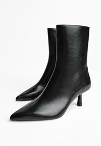 Zwarte enkellaarsjes van glad synthetisch materiaal, met een spitse neus, slanke hak en verticale naden voor een gestroomlijnd ontwerp.