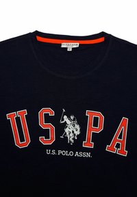 Černé tričko s krátkým rukávem s červeným nápisem "U.S. PA" a grafikou bílého pólisty. Kulatý výstřih s červeným akcentem uvnitř límce.