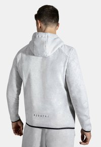 Lys grå hettegenser med teksturert overflate, med stor hette, kontrasterende svarte detaljer og en logo på nedre del av ryggen.