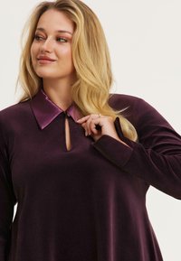Pruimenvelvet jurk met een satijnen paarse kraag, met een sleutelgatopening en lange mouwen. Zorgt voor een gladde textuur en een comfortabele pasvorm.