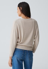 Beige gestreifter Pullover mit langen Ärmeln, Rundhalsausschnitt, strukturiertem Stoff und lockerer Passform, kombiniert mit blauen Denim-Jeans.