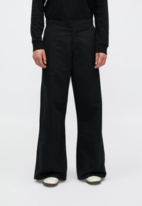 Pantaloni neri a gamba larga realizzati in misto cotone, caratterizzati da una texture liscia, due tasche frontali e sottili dettagli di cucitura verticale.