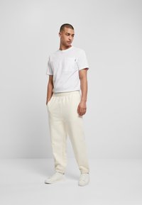 Tricou alb din bumbac cu un buzunar pe piept, asortat cu pantaloni de trening crem, cu talie elastică și manșete, completând ținuta cu adidași albi.