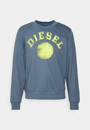 Sweat-shirt bleu à manches longues avec poignets et ourlet côtelés, comportant un cercle jaune délavé et le texte « DIESEL » sur la poitrine.