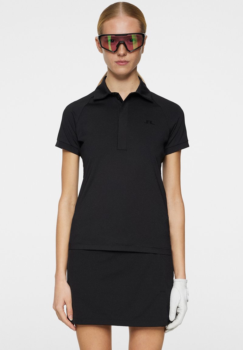 Czarna koszulka golfowa z krótkim rękawem, dopasowany krój i pasująca spódnica. Posiada subtelne logo oraz gładki, teksturowany materiał.