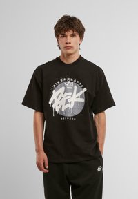 Sort bomulds T-shirt med korte ærmer, prydet med hvid graffiti-inspireret tryk med cirkulært design og tekst. Løs og afslappet pasform.