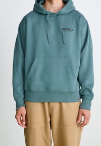 Sudadera con capucha en un verde azulado apagado con bolsillo canguro, puños y dobladillo acanalados. Presenta el logo 'Dickies' en gris oscuro en el pecho.