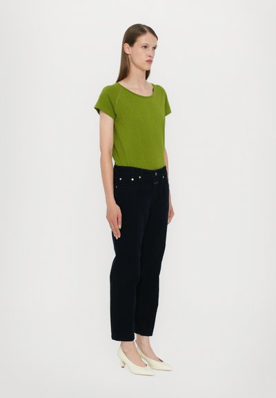 Green short-sleeve top, black pants with front pockets, white low-heeled shoes, smooth textures, simple design, standing pose against a white backdrop.