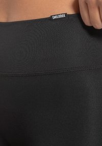 Leggings neri realizzati in un materiale liscio ed elastico, con una evidente cucitura a vista e un piccolo etichetta con la scritta "SMILODON" sulla vita.