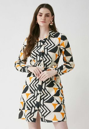 Knapparklänning med ett geometriskt mönster i svart, vitt och orange. Långa ärmar med manschetter och knytning i midjan. Tyget ser slätt ut.