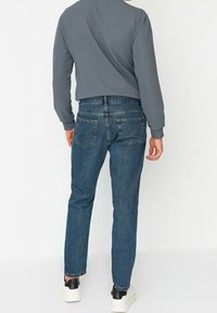 Vaqueros azules de mezclilla con corte recto, diseño de cinco bolsillos y costuras visibles. Se combinan con una camiseta gris de manga larga y zapatillas blancas.