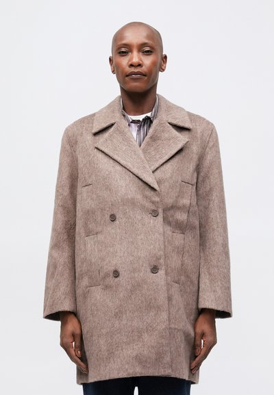 Manteau en laine marron à double boutonnage, avec un col cranté, des poches latérales et une finition douce et texturée. Porté sur une chemise rayée, en coupe décontractée.