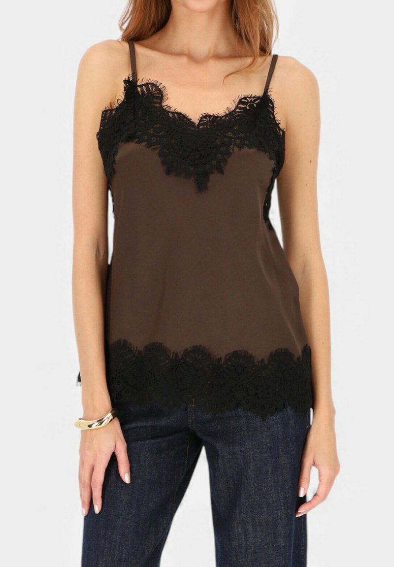 Kobieta ubrana w brązowy top bez rękawów z czarną koronkową lamówką na dekolcie i dole, zestawiony z ciemnoniebieskimi dżinsami i złotą bransoletką.