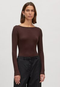 Bruine langemouwen bodysuit van een gladde stof met een brede halslijn, gecombineerd met zwarte, op maat gemaakte broeken. Eenvoudig en aansluitend ontwerp.