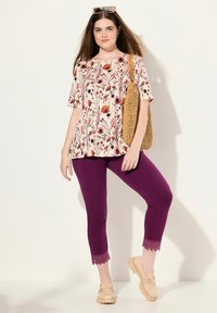 Haut à manches courtes à motif floral en crème avec des accents rouges et roses, associé à un pantalon violet longueur cheville avec finition en dentelle et des chaussures beiges.